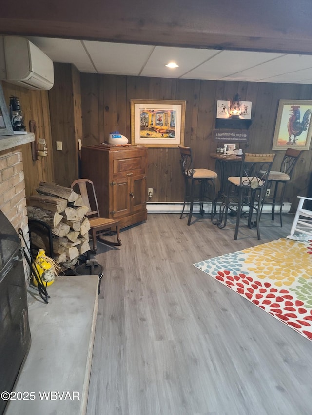 dining space with wood walls, a fireplace, a wall mounted AC, and light wood-type flooring