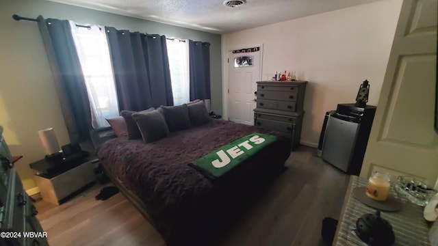 bedroom featuring wood-type flooring, stainless steel refrigerator, and a textured ceiling