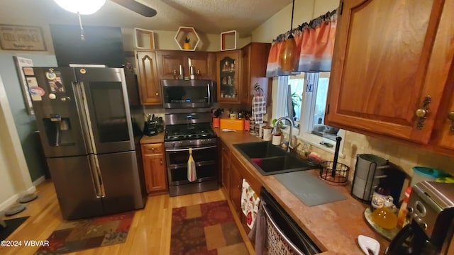 kitchen with appliances with stainless steel finishes, sink, ceiling fan, a textured ceiling, and light hardwood / wood-style flooring