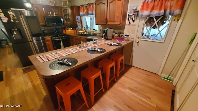 kitchen with stainless steel refrigerator, a breakfast bar, hanging light fixtures, gas range oven, and kitchen peninsula