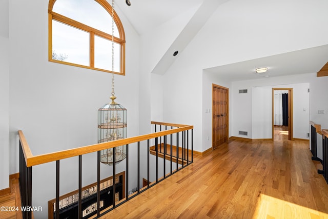 hall with a chandelier, wood-type flooring, and high vaulted ceiling