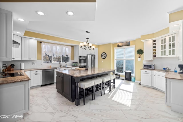 kitchen with pendant lighting, appliances with stainless steel finishes, a kitchen island, light stone counters, and white cabinetry