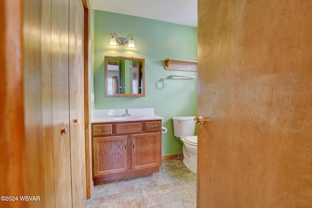 bathroom with baseboards, toilet, vanity, and stone tile floors