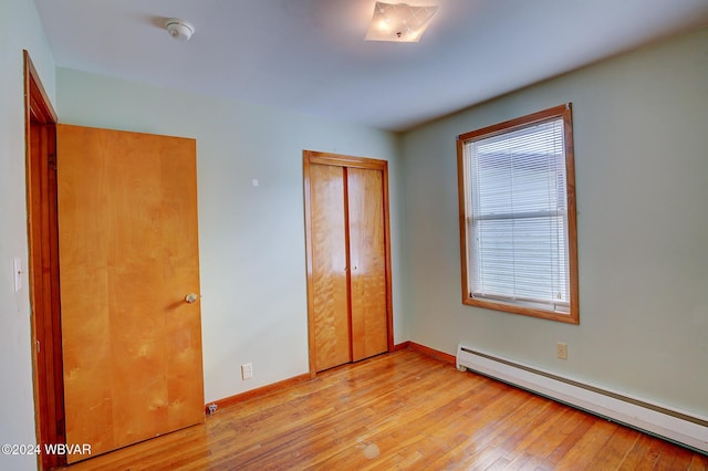 unfurnished bedroom with light wood-style flooring, baseboards, baseboard heating, and a closet