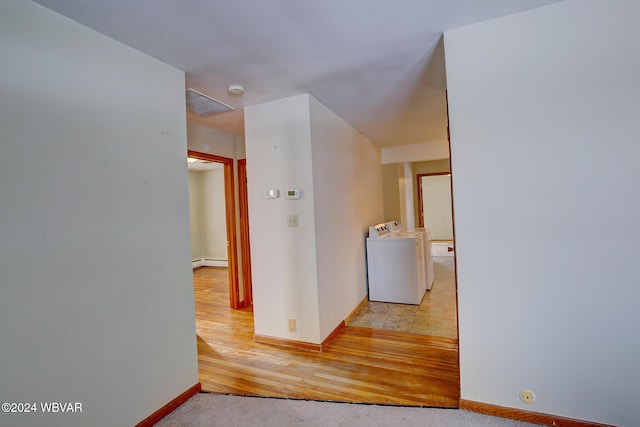 hallway featuring light carpet, baseboards, a baseboard radiator, washing machine and clothes dryer, and light wood-type flooring