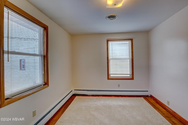 empty room with a baseboard heating unit, a wealth of natural light, visible vents, and dark wood finished floors