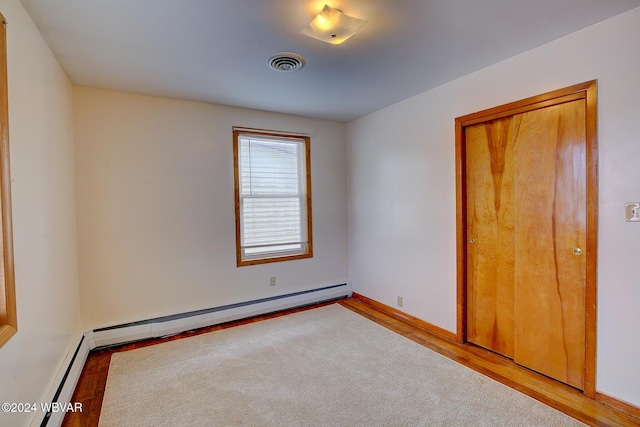 spare room featuring a baseboard radiator, visible vents, baseboard heating, wood finished floors, and baseboards