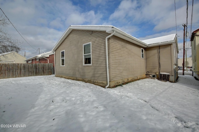 view of snowy exterior featuring central AC and fence