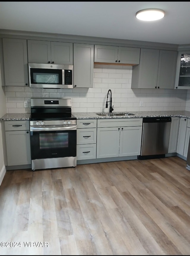 kitchen with sink, light stone counters, decorative backsplash, appliances with stainless steel finishes, and light wood-type flooring