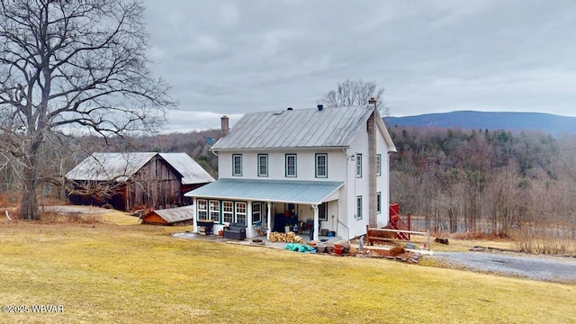 view of front facade with a mountain view, metal roof, a front yard, and a view of trees