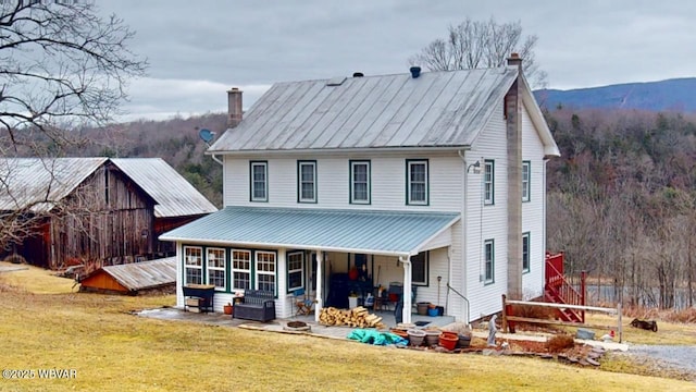 view of front of house featuring a patio, a front yard, a forest view, a chimney, and metal roof