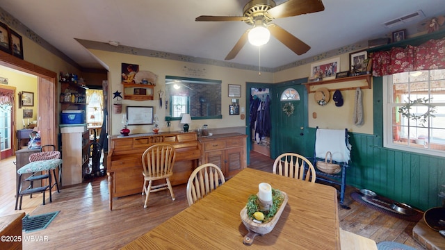 dining room with a wainscoted wall, light wood-style flooring, visible vents, and ceiling fan