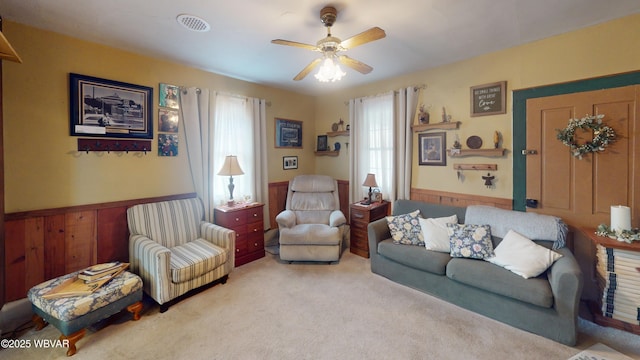 carpeted living room featuring a wainscoted wall, wooden walls, visible vents, and a ceiling fan