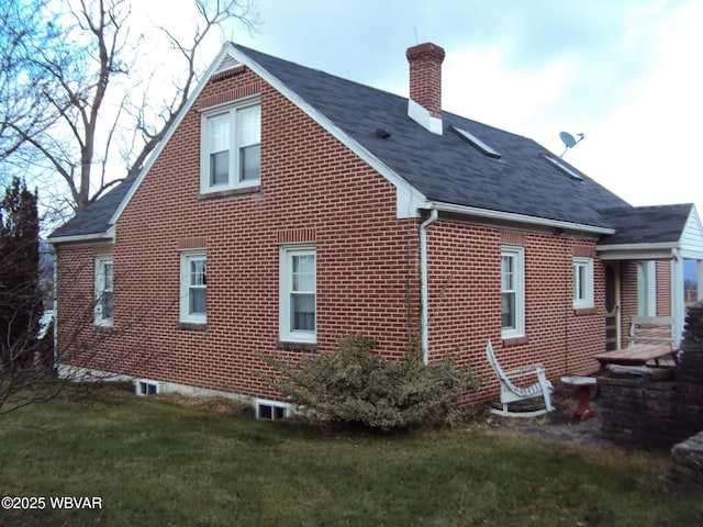 rear view of property featuring a chimney, brick siding, a yard, and roof with shingles