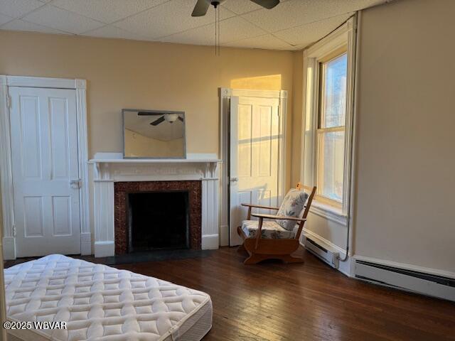 bedroom with a drop ceiling, ceiling fan, a fireplace with flush hearth, and wood finished floors