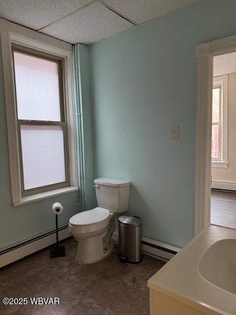 bathroom with a baseboard heating unit, toilet, and a drop ceiling