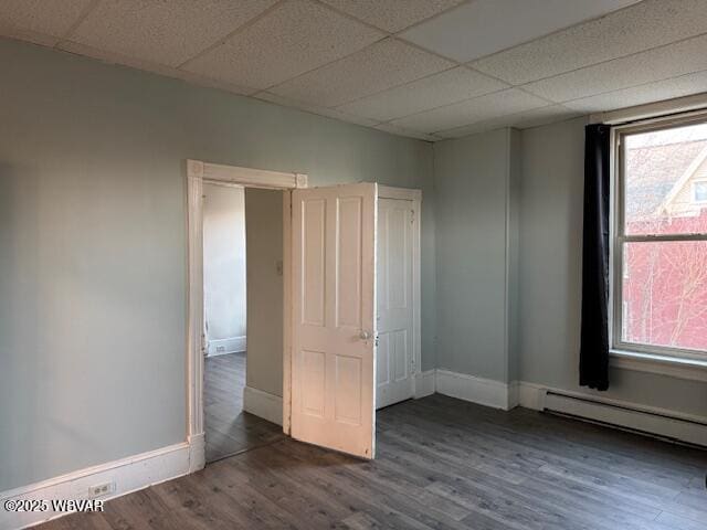 empty room with baseboard heating, a paneled ceiling, baseboards, and wood finished floors