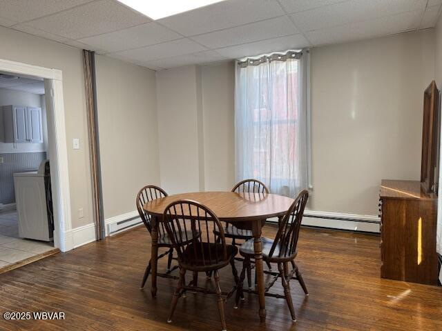 dining area with a paneled ceiling, baseboard heating, washer / dryer, and wood finished floors