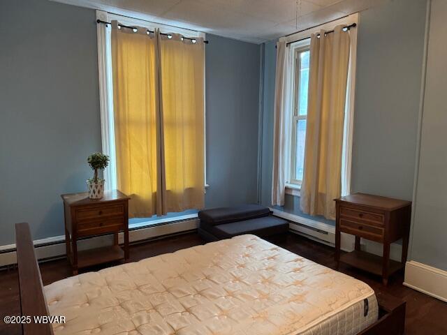 bedroom with a baseboard heating unit, baseboards, and wood finished floors