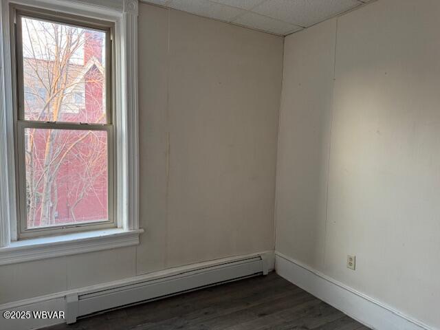 empty room featuring dark wood-style floors, a baseboard heating unit, and a paneled ceiling