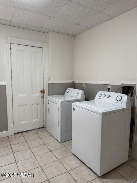 clothes washing area featuring light tile patterned floors, laundry area, washer and dryer, and wainscoting