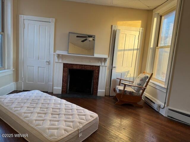 bedroom featuring a baseboard heating unit, dark wood-type flooring, a fireplace with flush hearth, and baseboards