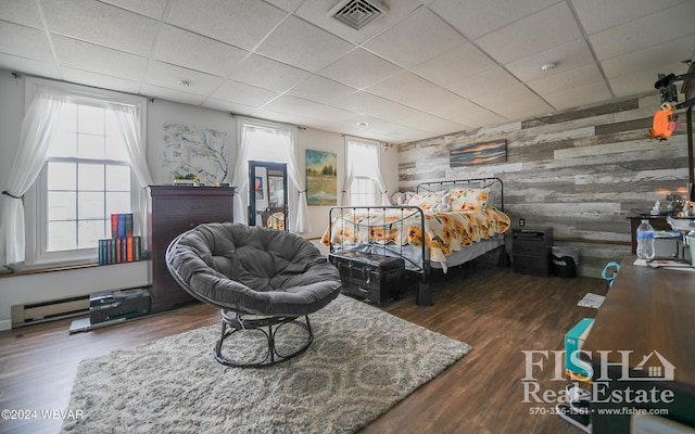 bedroom featuring wooden walls, a drop ceiling, dark wood-type flooring, and a baseboard heating unit