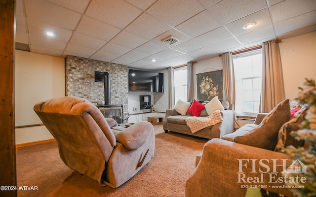 living room with a drop ceiling, light colored carpet, and a wood stove