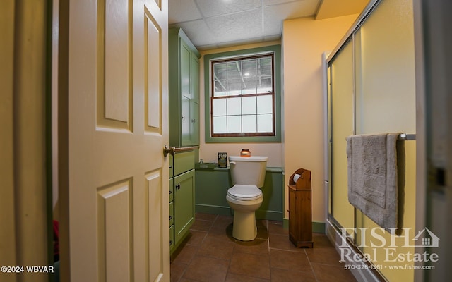 bathroom featuring a paneled ceiling, a shower with door, tile patterned flooring, and toilet