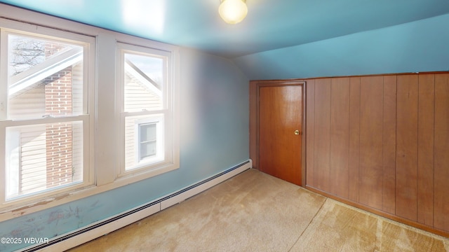 unfurnished bedroom with lofted ceiling, a baseboard radiator, wooden walls, a closet, and light colored carpet