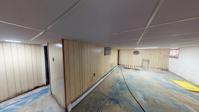 basement with a baseboard heating unit, a paneled ceiling, and wooden walls