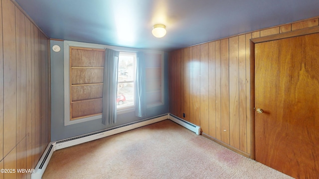 carpeted empty room featuring baseboard heating and wood walls