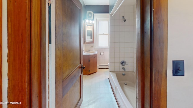 bathroom with vanity, a baseboard heating unit, tile walls, and tiled shower / bath