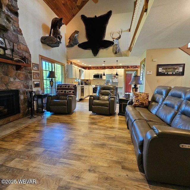 living area with light wood finished floors, high vaulted ceiling, and a stone fireplace
