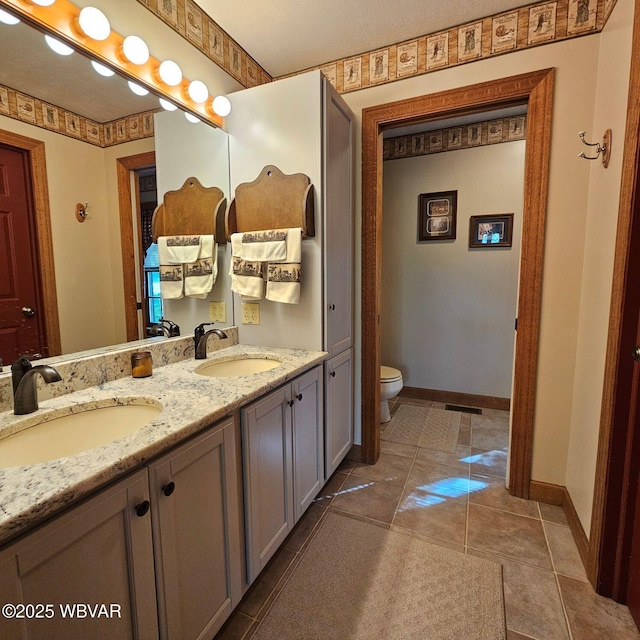 full bathroom with toilet, baseboards, and double vanity
