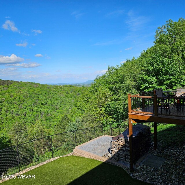view of yard with a wooded view, a deck, and fence