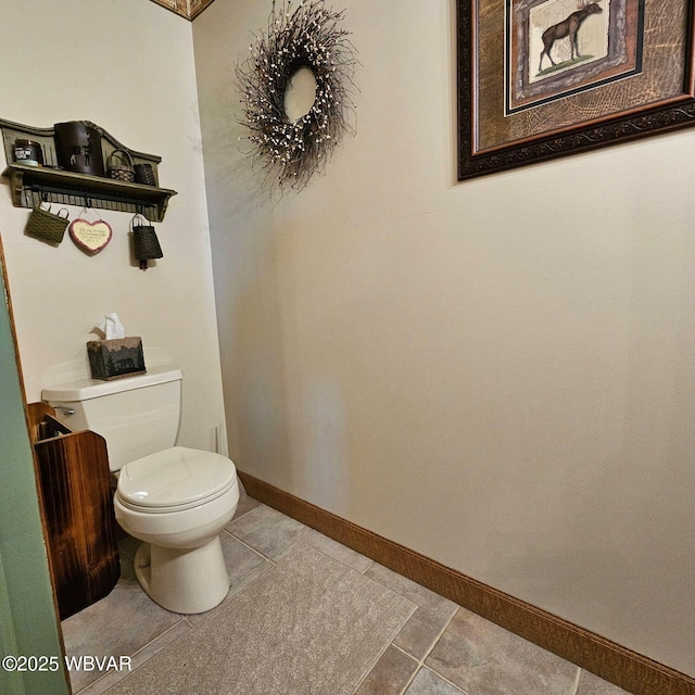 half bath featuring tile patterned flooring, toilet, and baseboards