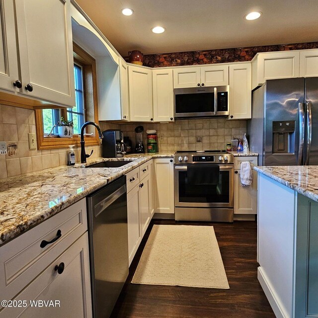 kitchen with stainless steel appliances, a sink, dark wood-type flooring, light stone counters, and white cabinetry
