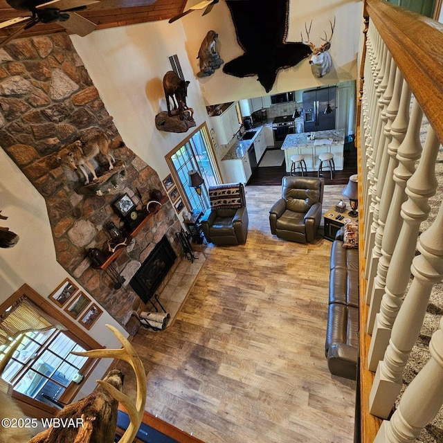 living room with wood finished floors, a high ceiling, a fireplace, and a ceiling fan