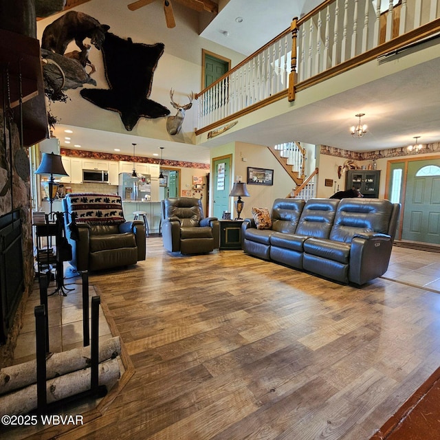 living room with a high ceiling, light wood-type flooring, stairway, a chandelier, and a fireplace