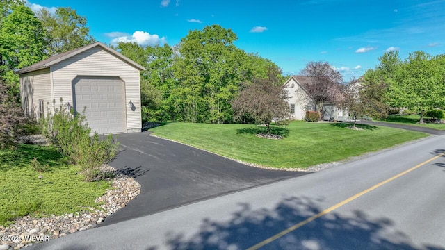 view of property exterior with asphalt driveway, a lawn, a detached garage, and an outbuilding
