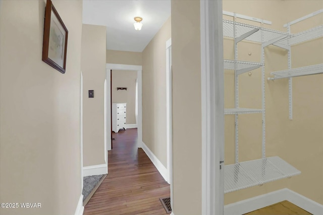 hall featuring visible vents, baseboards, and hardwood / wood-style flooring