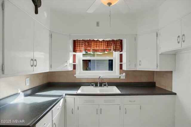 kitchen with dark countertops, white cabinetry, and a sink