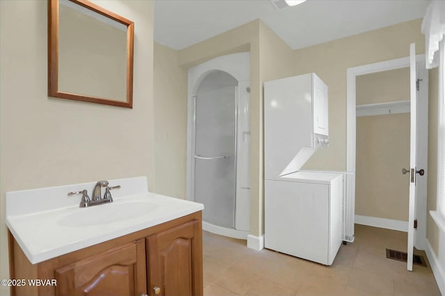 full bath with tile patterned floors, visible vents, stacked washer and clothes dryer, a stall shower, and vanity