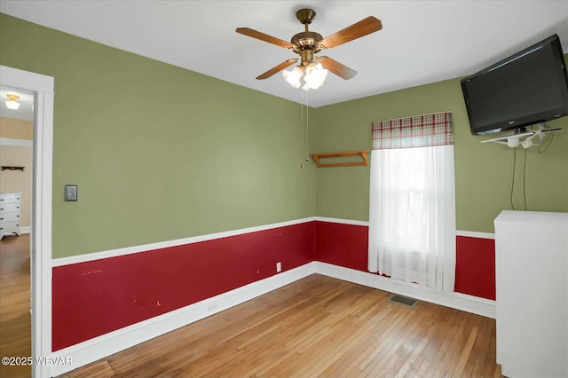 empty room with ceiling fan, visible vents, baseboards, and hardwood / wood-style floors