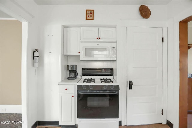 kitchen with white microwave, white cabinetry, light countertops, and gas range oven