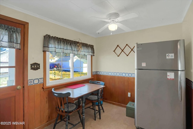 dining room with a wealth of natural light, wood walls, wainscoting, and ceiling fan