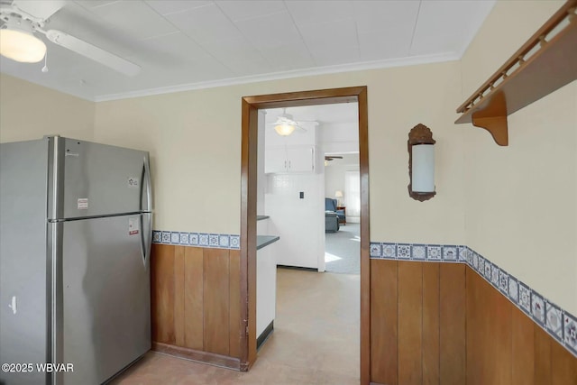 kitchen with a wainscoted wall, crown molding, freestanding refrigerator, and ceiling fan