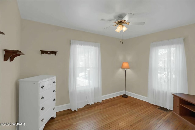 unfurnished bedroom featuring multiple windows, baseboards, light wood-style floors, and ceiling fan