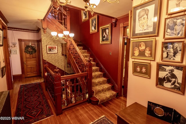 staircase with crown molding, a chandelier, and hardwood / wood-style floors